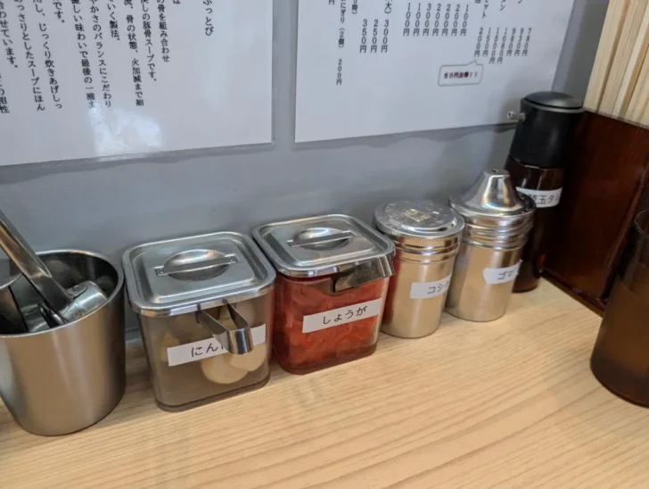 卓上にはにんにく、しょうが、コショウ、ゴマ、替玉タレとスタンダードな味変あり